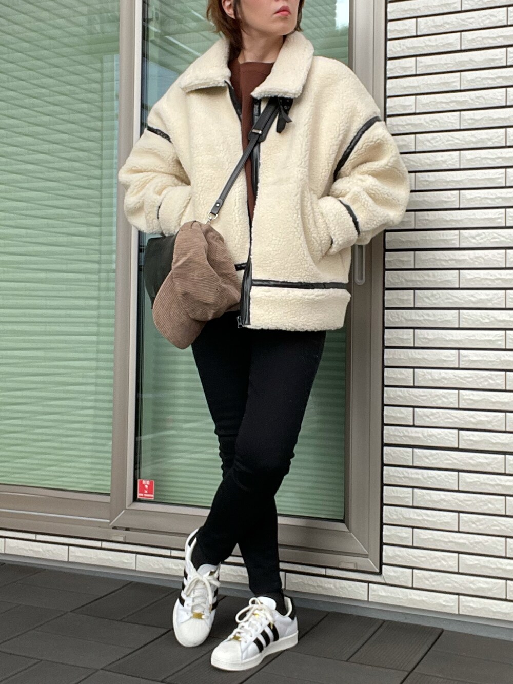 ブラック系のムートンコート、ブラウン系のスウェット、ブラック系のデニムパンツを着用したレディースの冬コーディネートの2枚目の写真