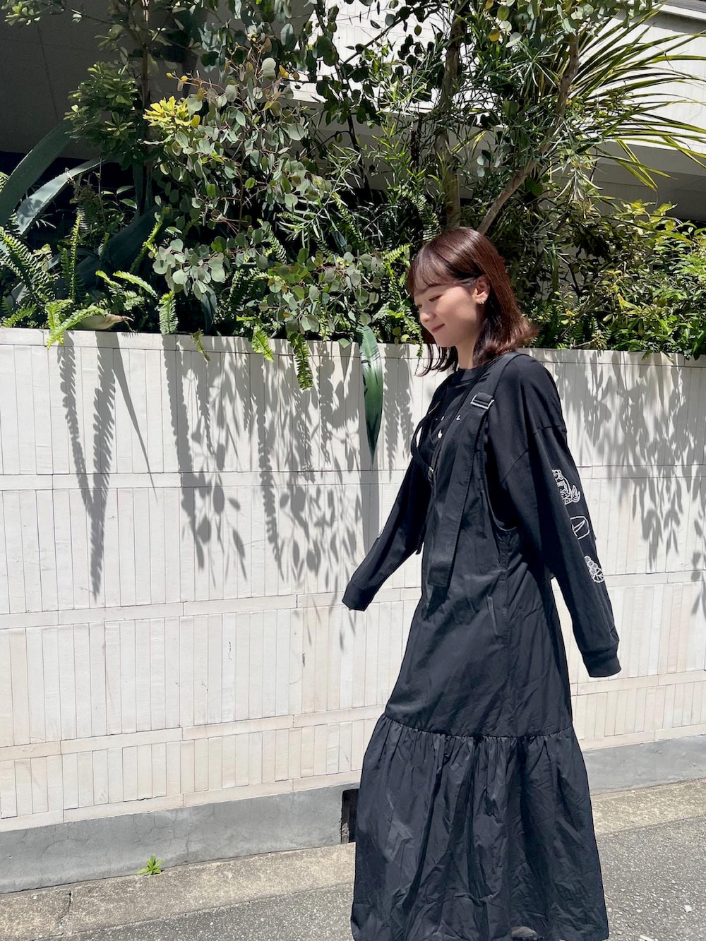 ブラック系のジャンパースカート、ブラック系のTシャツ/カットソー、ベージュ系のスニーカーを着用したレディースの春コーディネートの2枚目の写真