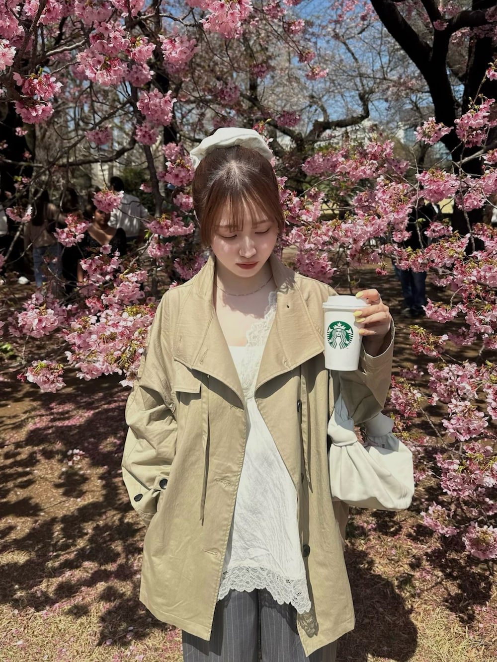 ホワイト系のキャミソール、ベージュ系のトレンチコート、グレー系のスラックスを着用したレディースの春コーディネートの2枚目の写真