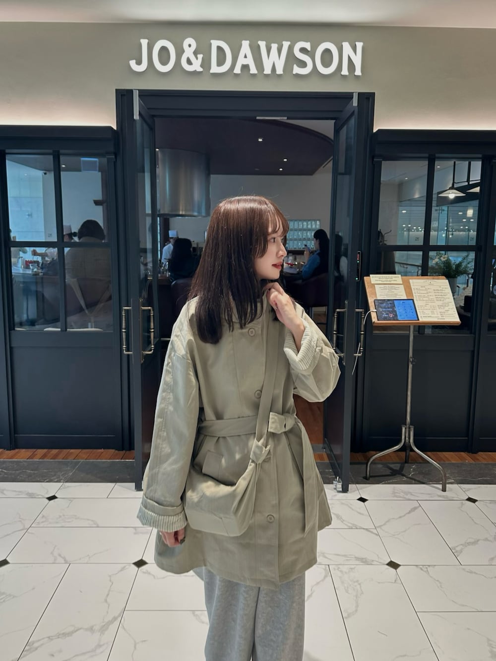 グレー系のスウェットパンツ、ベージュ系のトレンチコート、ブラック系のスニーカーを着用したレディースの春コーディネートの2枚目の写真