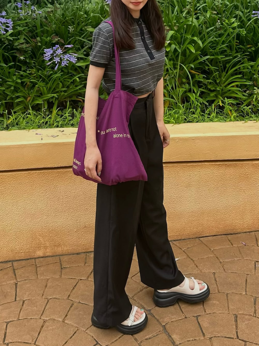 グレー系のポロシャツ、ブラック系のパンツ、パープル系のトートバッグを着用したレディースの夏コーディネートの2枚目の写真