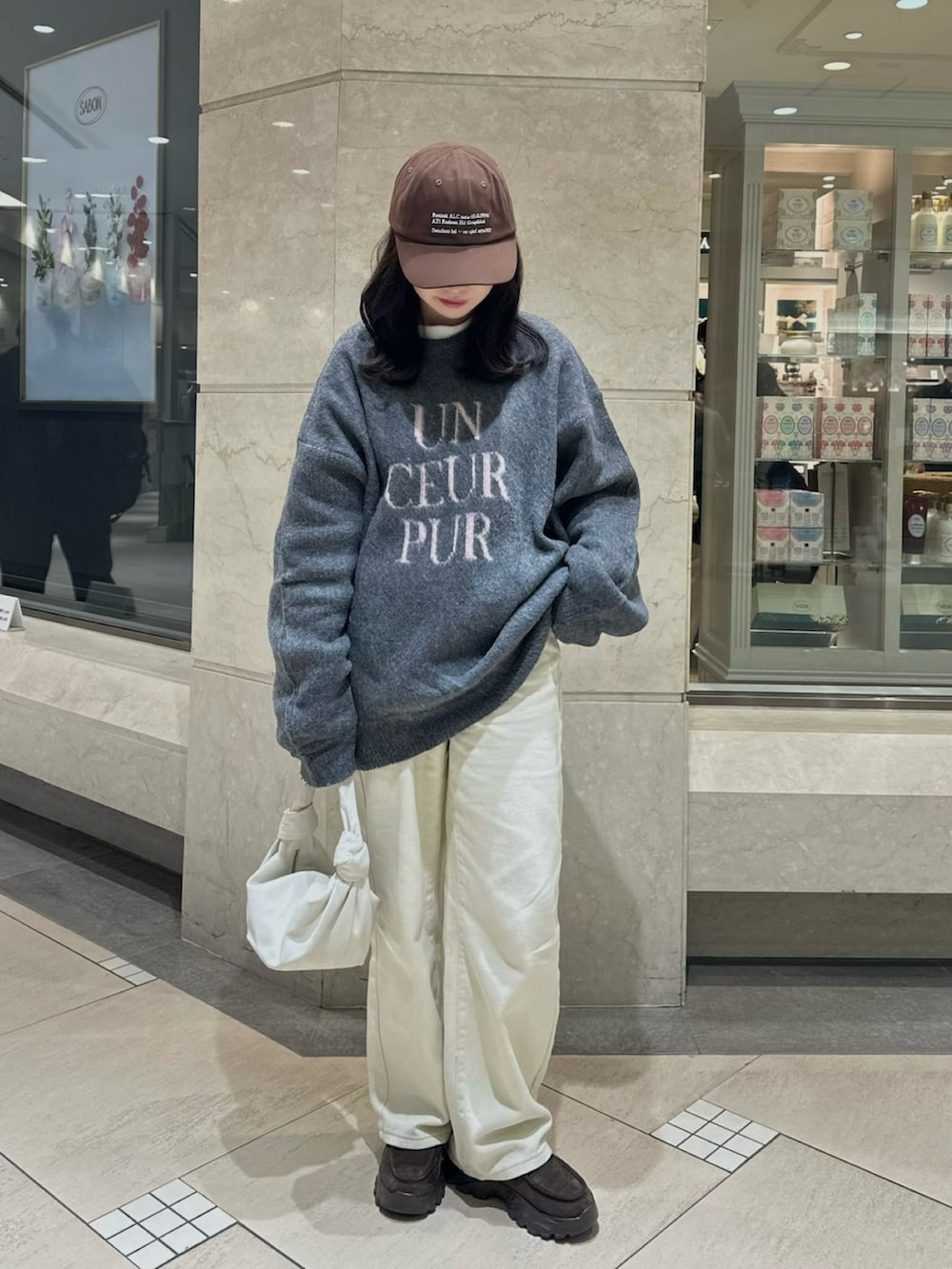 グレー系のニット/セーター、ブラウン系のローファー、ホワイト系のハンドバッグを着用したレディースの冬コーディネートの2枚目の写真