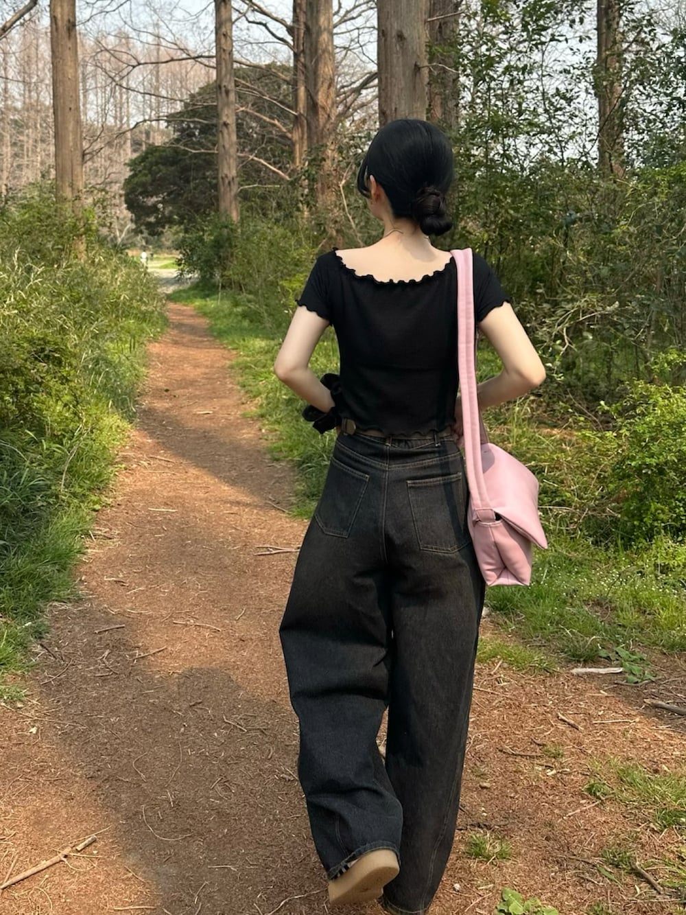 ブラック系のトップス、ブラック系のデニムパンツ、ピンク系のショルダーバッグを着用したレディースの春コーディネートの2枚目の写真