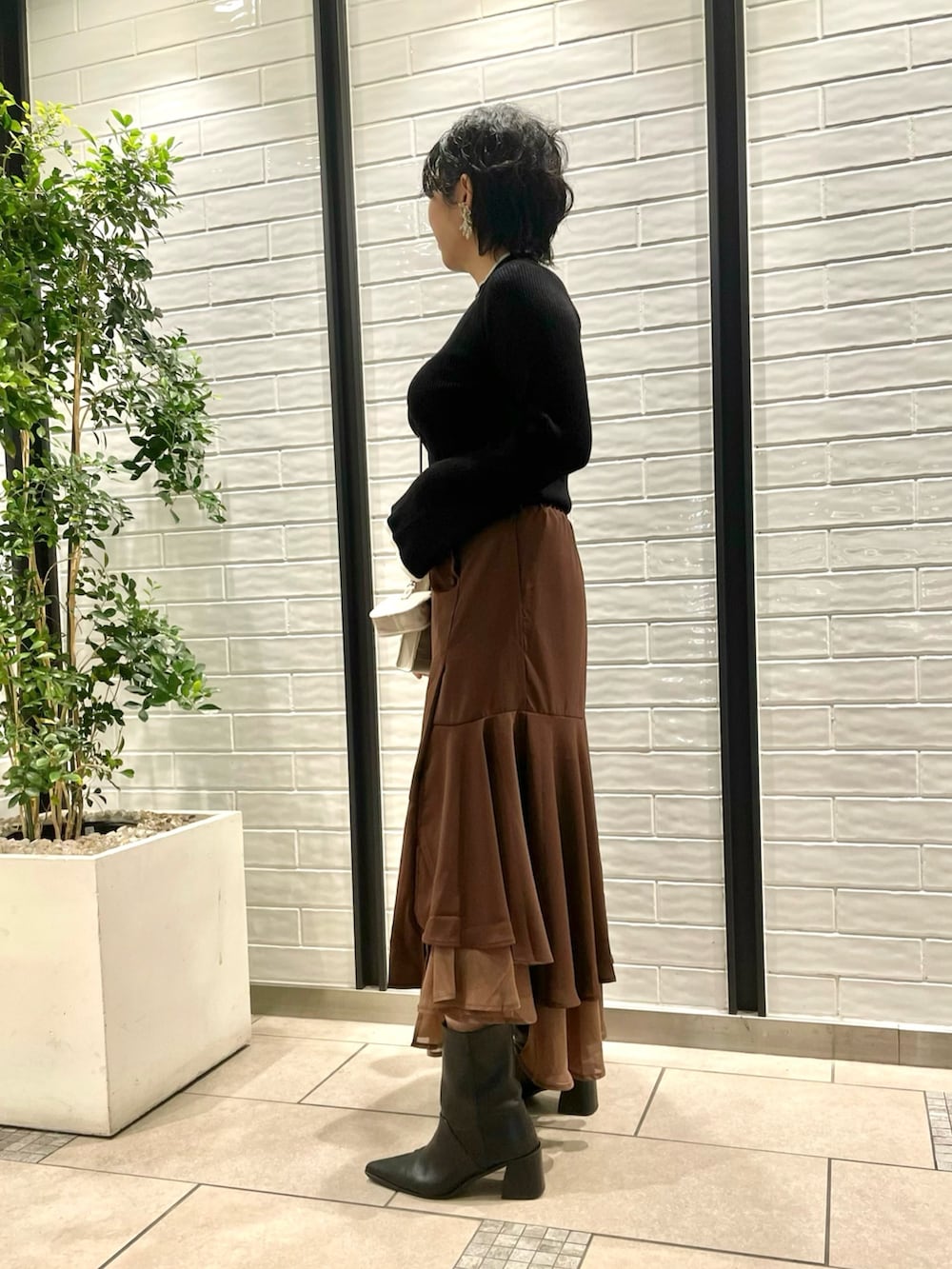 ブラック系のニット/セーター、ブラウン系のスカート、ベージュ系のショルダーバッグを着用したレディースの秋コーディネートの2枚目の写真