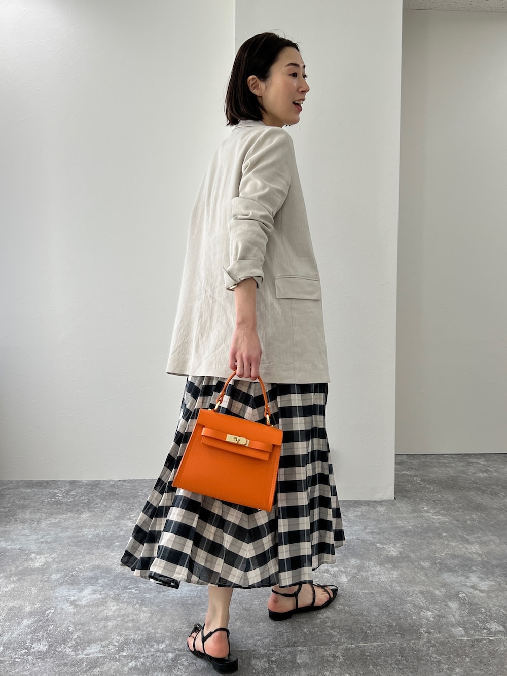 ベージュ系のテーラードジャケット、ブラック系のサンダル、オレンジ系のショルダーバッグを着用したレディースの冬コーディネートの2枚目の写真