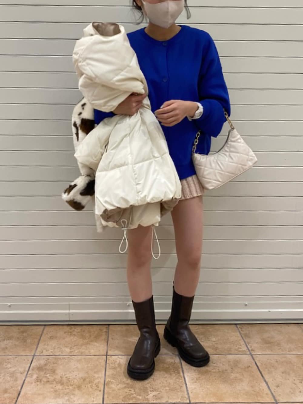 ホワイト系のハンドバッグ、ブラウン系のブーツ、ホワイト系のブルゾンを着用したレディースの冬コーディネートの2枚目の写真