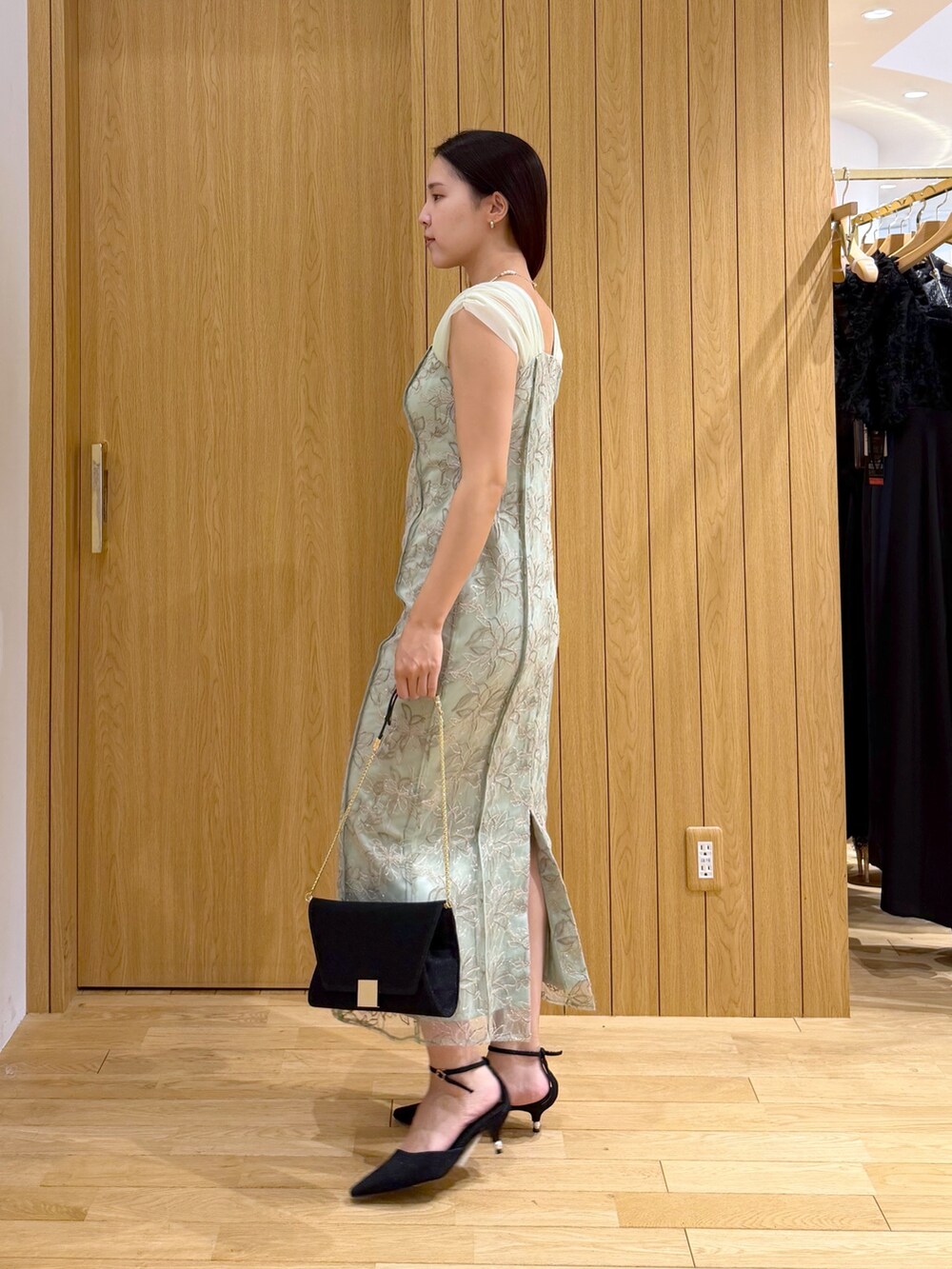 ブラック系のパンプス、ブラック系のクラッチバッグ、グリーン系のワンピースを着用したレディースの夏コーディネートの2枚目の写真