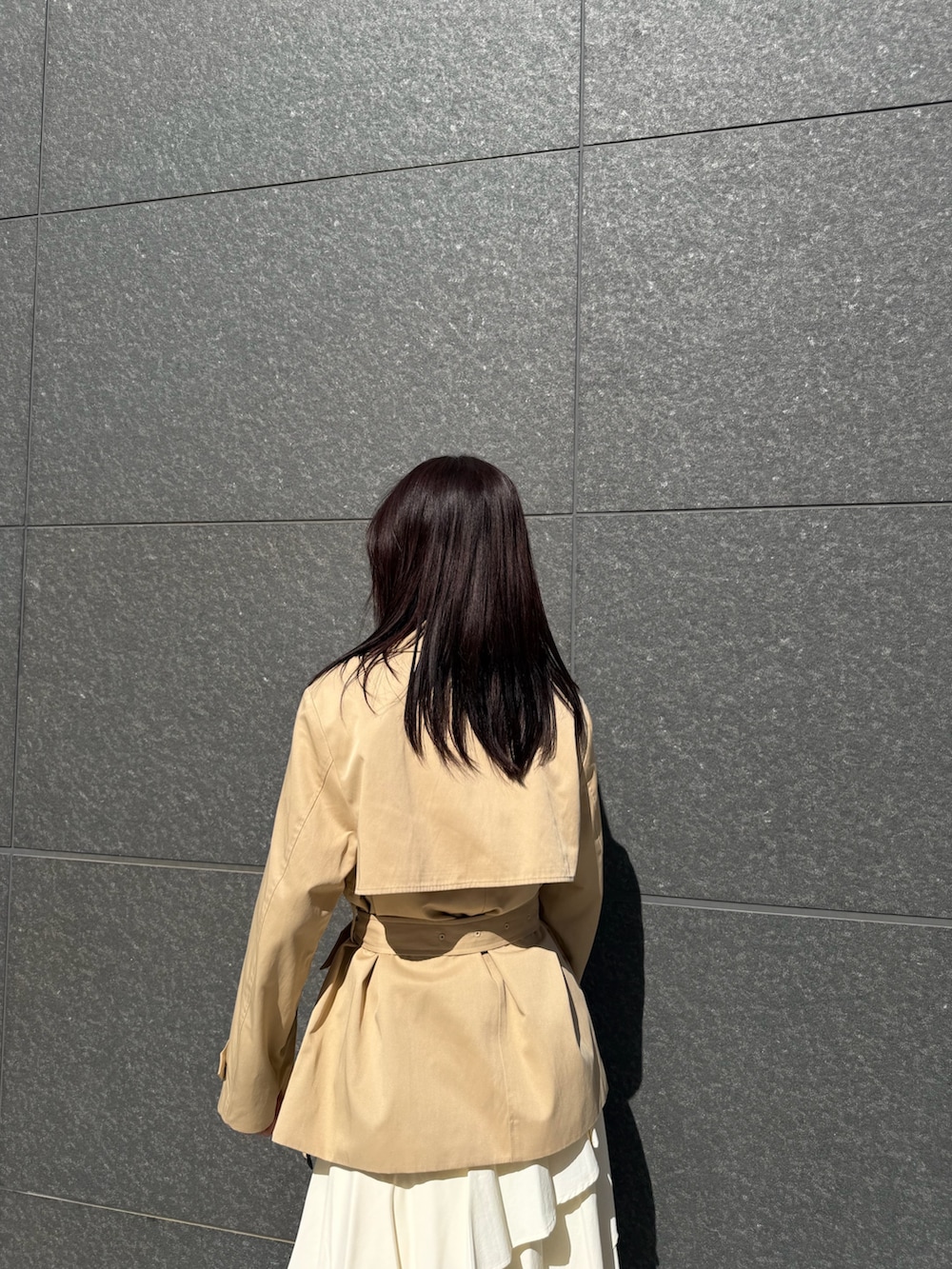 ベージュ系のトレンチコート、ホワイト系のスカート、ブラウン系のハンドバッグを着用したレディースの冬コーディネートの6枚目の写真