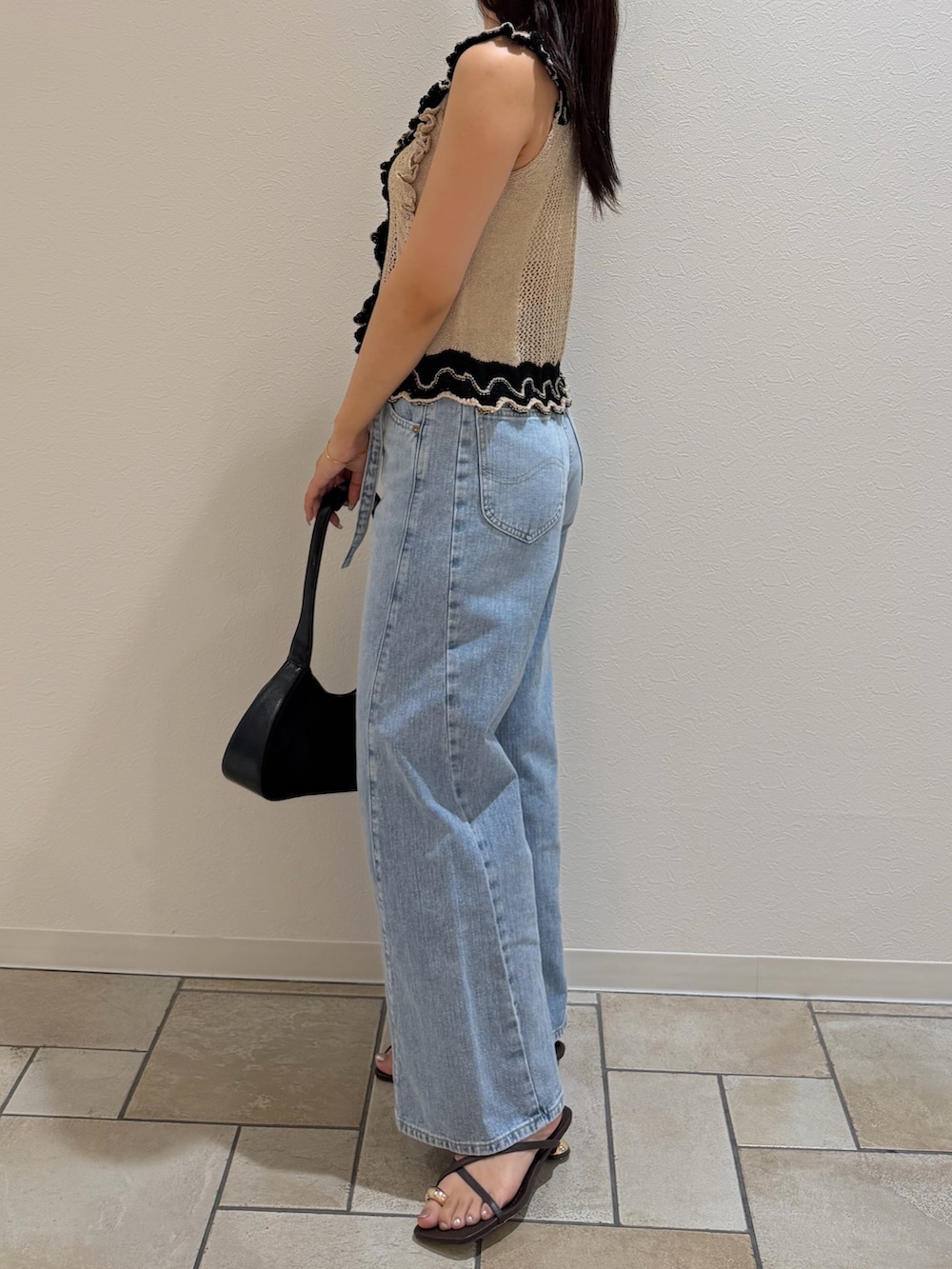 ブルー系のデニムパンツ、ベージュ系のニット/セーター、ブラック系のハンドバッグを着用したレディースの夏コーディネートの2枚目の写真