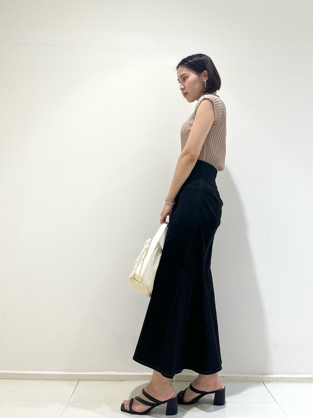 ブラック系のスカート、ベージュ系のニット/セーター、ホワイト系のハンドバッグを着用したレディースの夏コーディネートの2枚目の写真