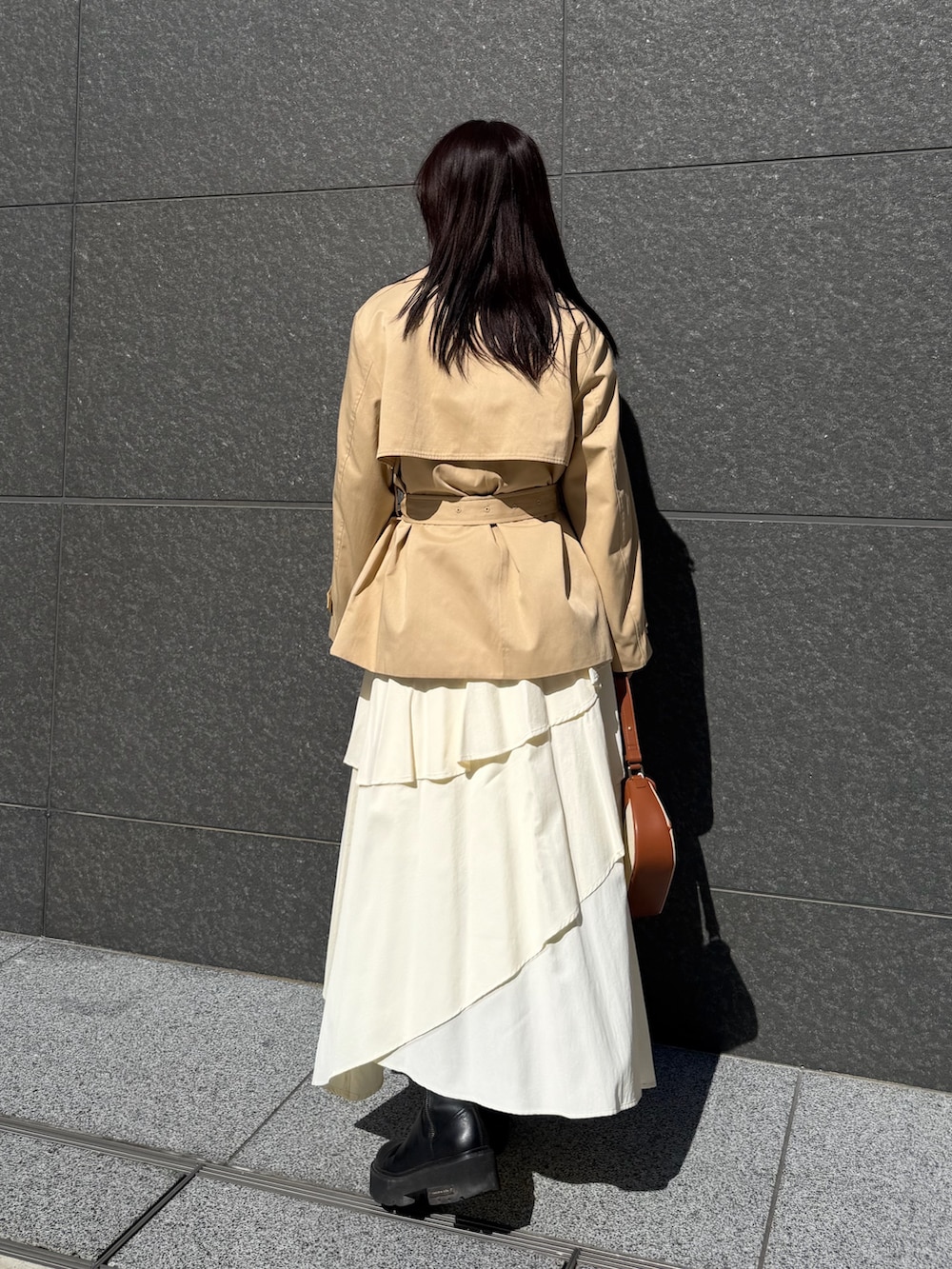 ベージュ系のトレンチコート、ホワイト系のスカート、ブラウン系のハンドバッグを着用したレディースの冬コーディネートの3枚目の写真
