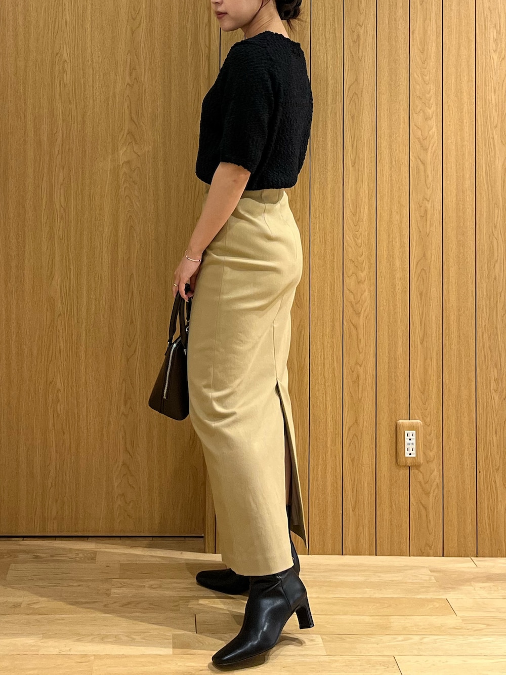 ブラック系のブーツ、ベージュ系のスカート、ブラウン系のボストンバッグを着用したレディースの秋コーディネートの2枚目の写真