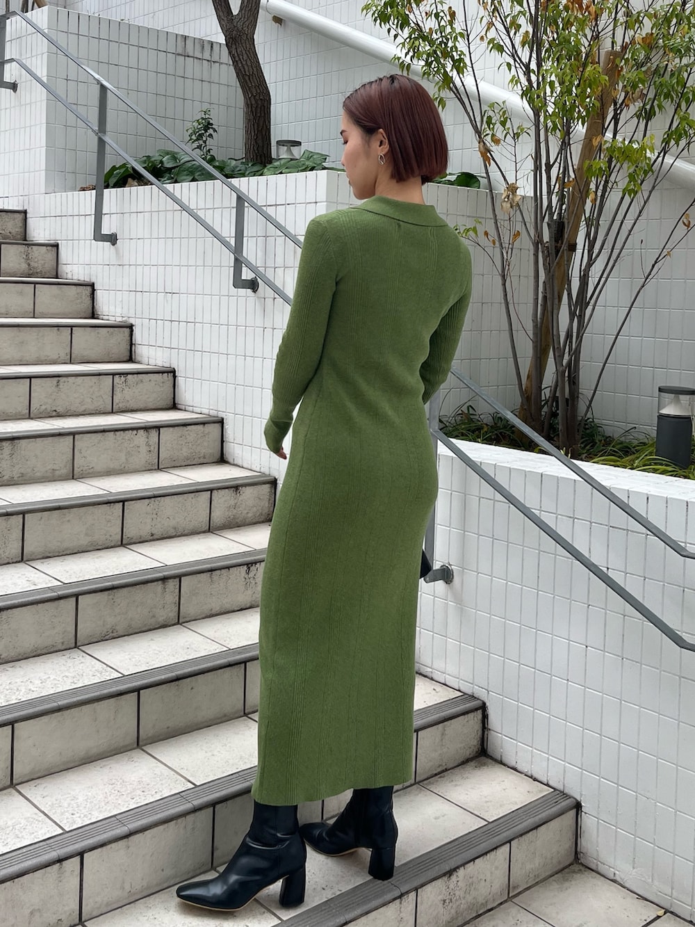 ブラック系のブーツ、ブラック系のハンドバッグ、グリーン系のワンピースを着用したレディースの冬コーディネートの3枚目の写真