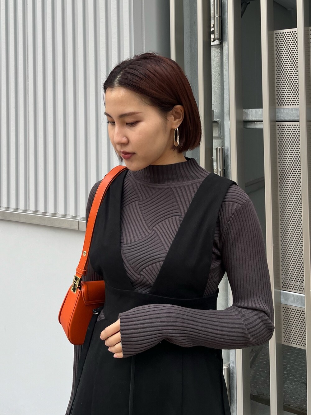 グレー系のニット/セーター、ブラック系のジャンパースカート、オレンジ系のショルダーバッグを着用したレディースの冬コーディネートの4枚目の写真