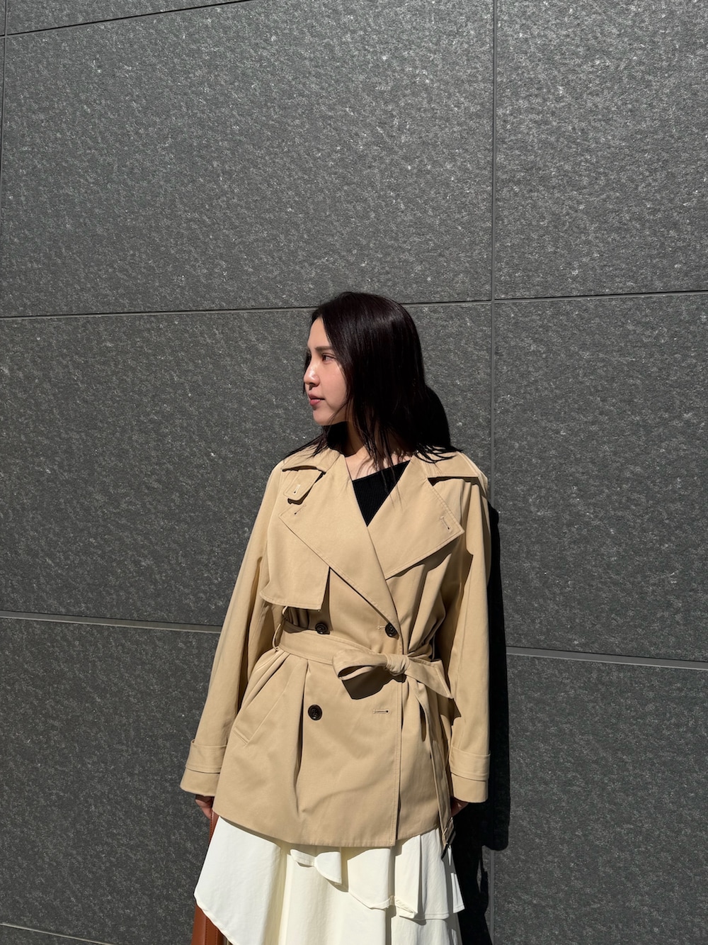 ベージュ系のトレンチコート、ホワイト系のスカート、ブラウン系のハンドバッグを着用したレディースの冬コーディネートの4枚目の写真