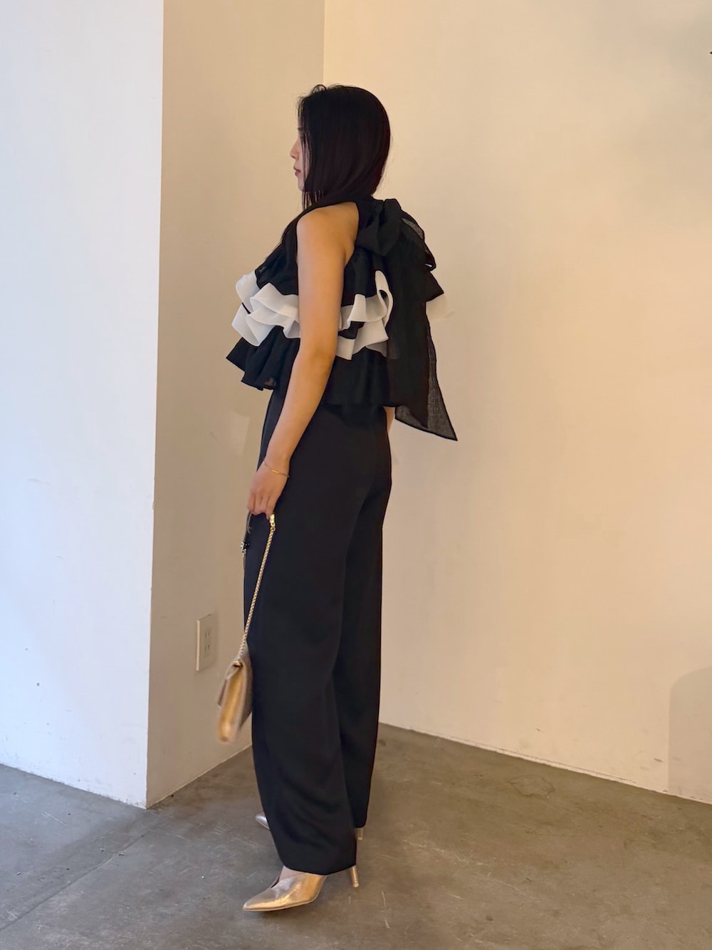 ブラック系のパンツドレス、ゴールド系のパンプス、ゴールド系のクラッチバッグを着用したレディースの夏コーディネートの2枚目の写真