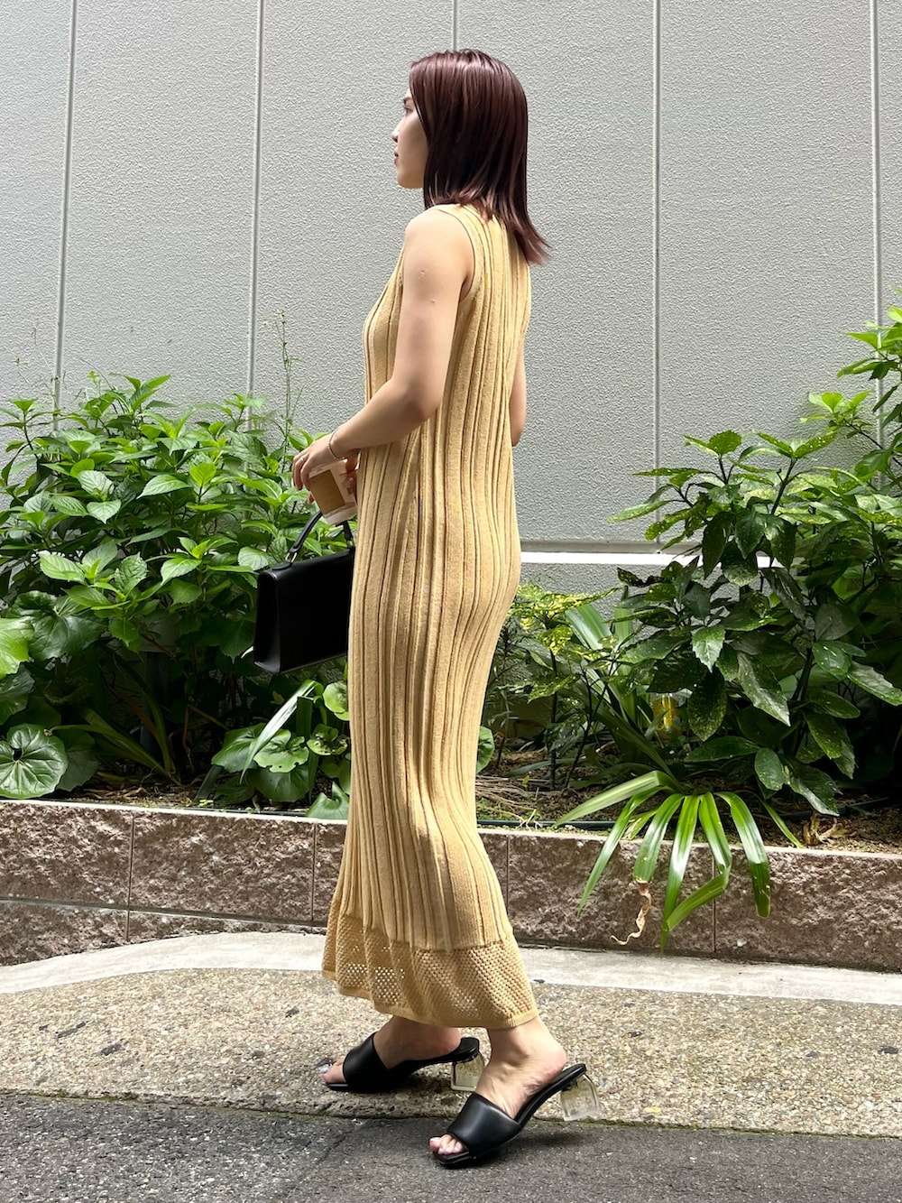 イエロー系のワンピース、ブラック系のハンドバッグ、ブラック系のサンダルを着用したレディースの夏コーディネートの2枚目の写真