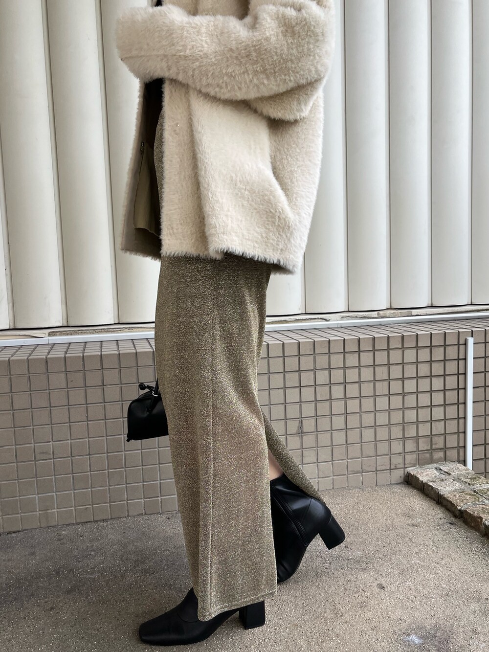 ホワイト系のカーディガン/ボレロ、ゴールド系のスカート、ブラック系のニット/セーターを着用したレディースの冬コーディネートの7枚目の写真