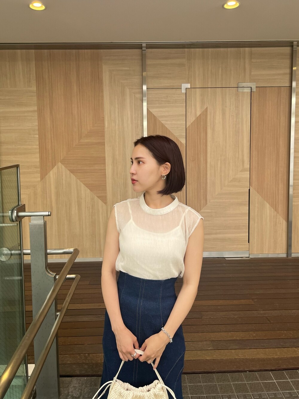 ブルー系のシャツ/ブラウス、ブルー系のデニムスカート、ベージュ系のハンドバッグを着用したレディースの夏コーディネートの2枚目の写真