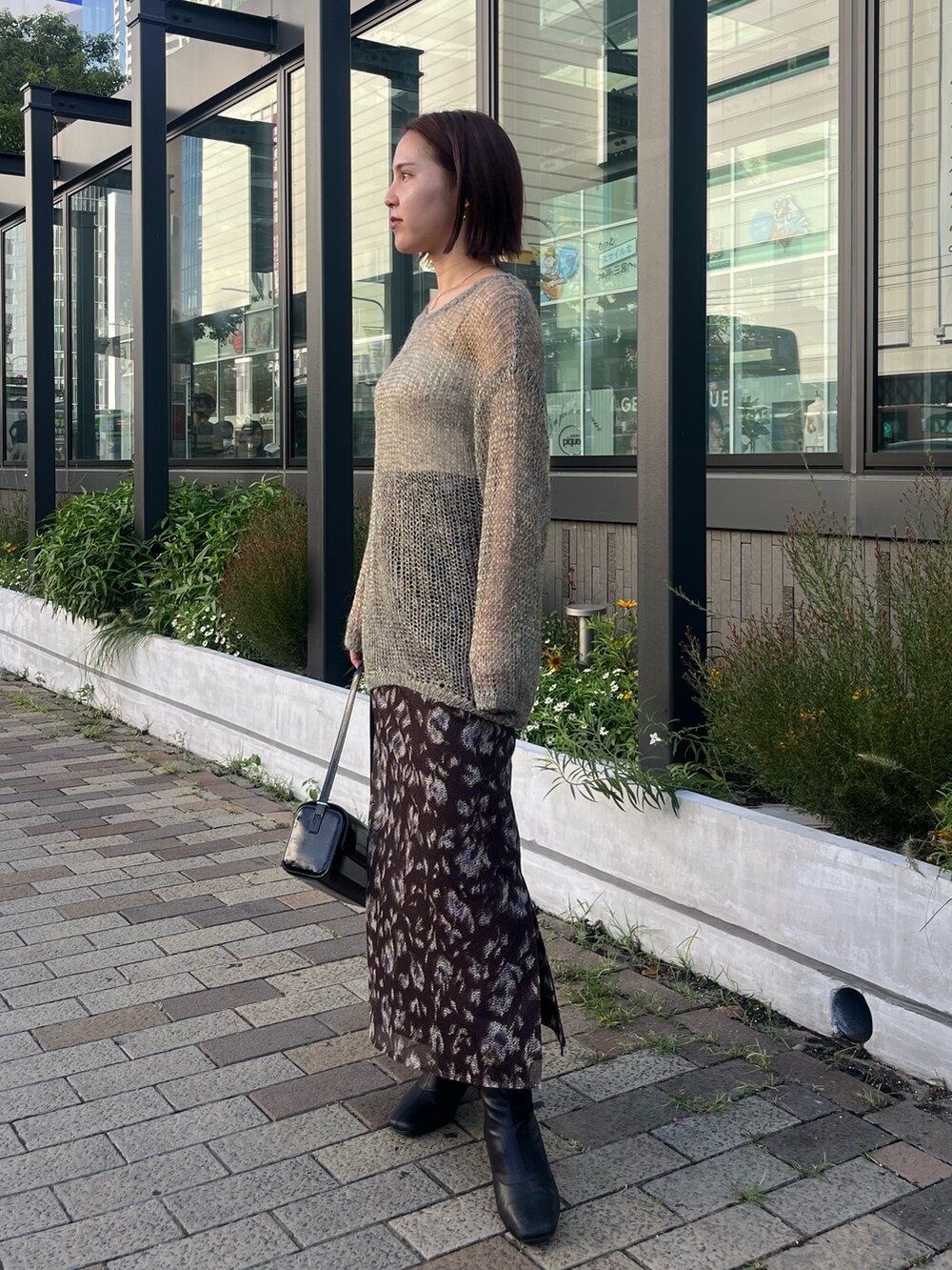 ブラック系のショルダーバッグ、グレー系のニット/セーター、ブラウン系のスカートを着用したレディースの秋コーディネートの2枚目の写真