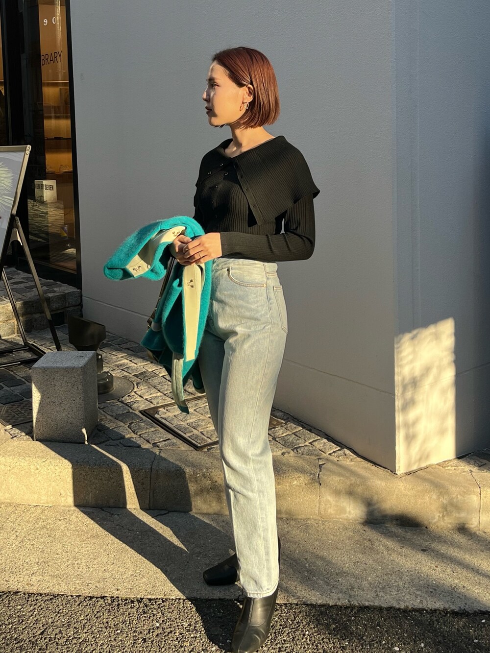 ブルー系のデニムパンツ、ブルー系のカーディガン/ボレロ、ブラック系のニット/セーターを着用したレディースの冬コーディネートの2枚目の写真