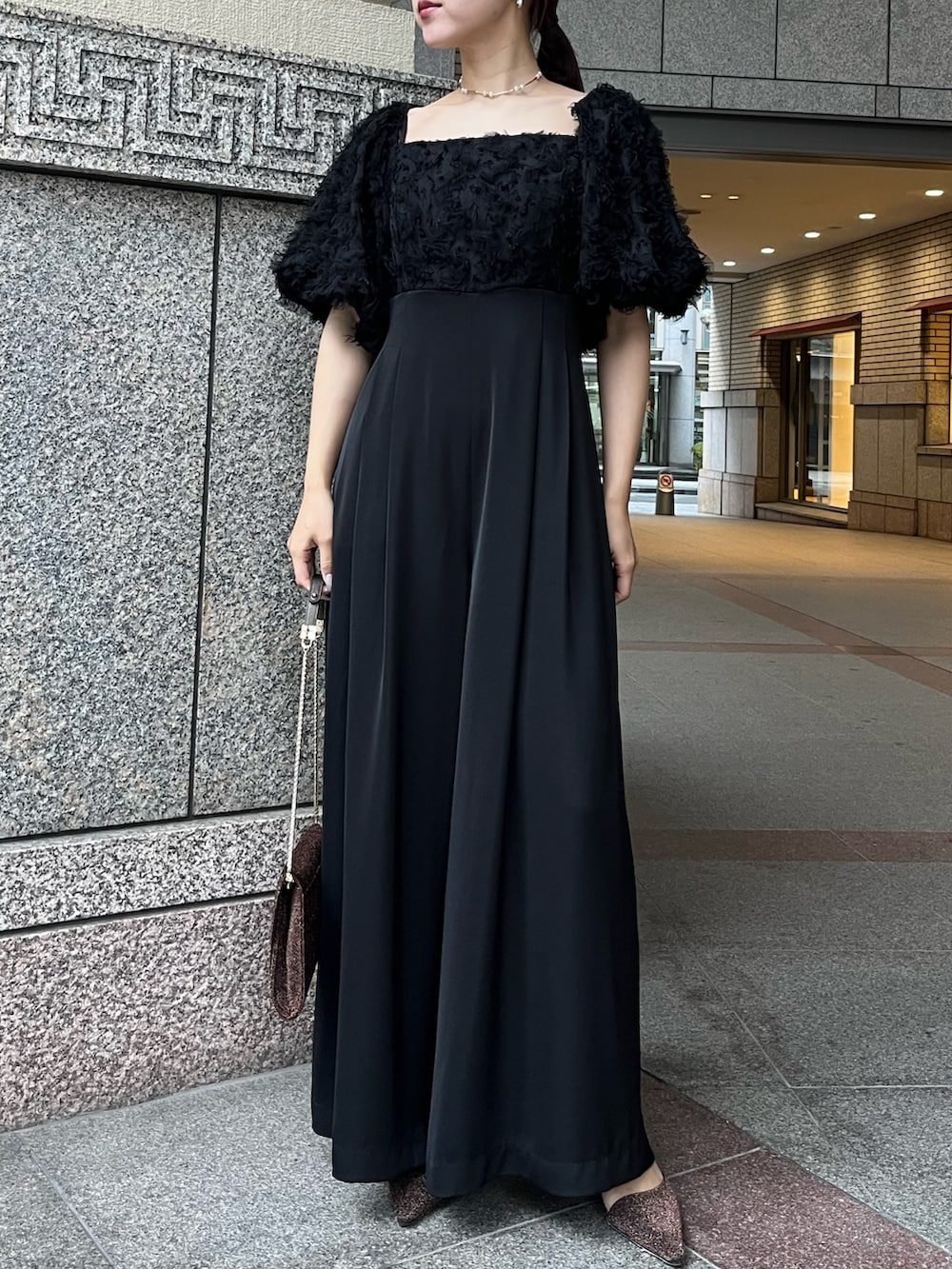 その他のパンプス、ブラック系のパンツドレス、その他のクラッチバッグを着用したレディースの冬コーディネートの2枚目の写真