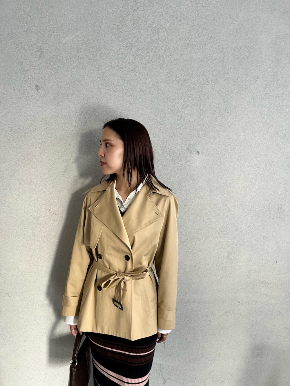 ブラウン系のハンドバッグ、ブラウン系のワンピース、ベージュ系のトレンチコートを着用したレディースの冬コーディネートの4枚目の写真