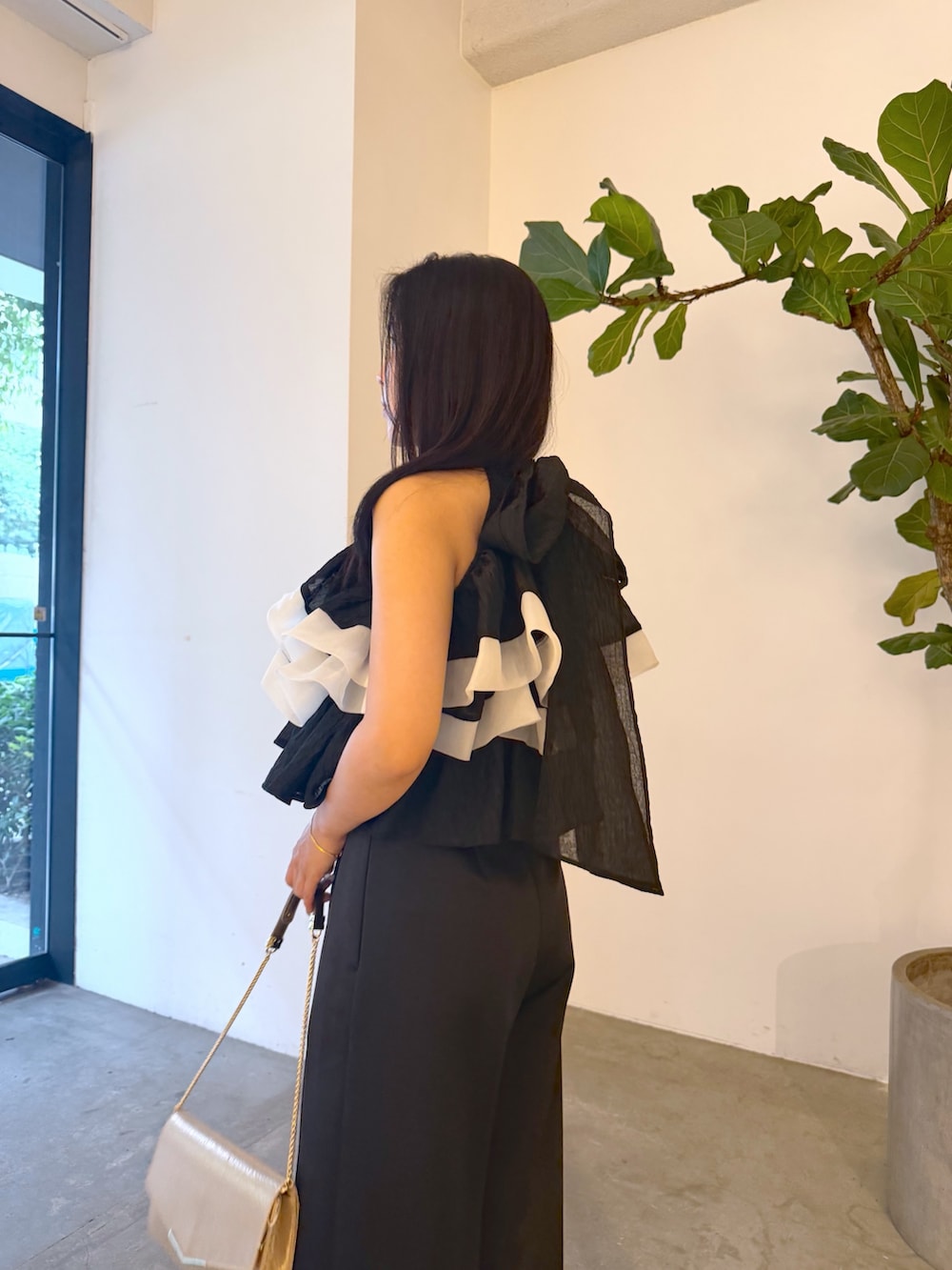 ブラック系のパンツドレス、ゴールド系のパンプス、ゴールド系のクラッチバッグを着用したレディースの夏コーディネートの5枚目の写真