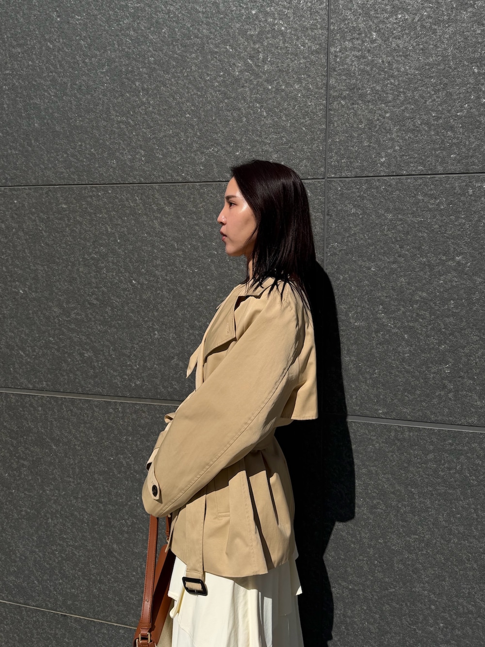 ベージュ系のトレンチコート、ホワイト系のスカート、ブラウン系のハンドバッグを着用したレディースの冬コーディネートの5枚目の写真