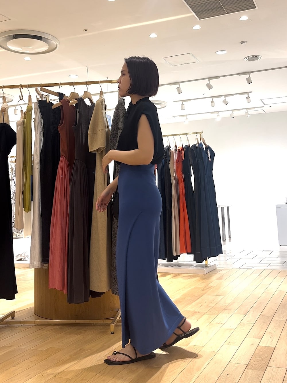 ブルー系のスカート、ブラック系のニット/セーター、ブラック系のショルダーバッグを着用したレディースの夏コーディネートの2枚目の写真