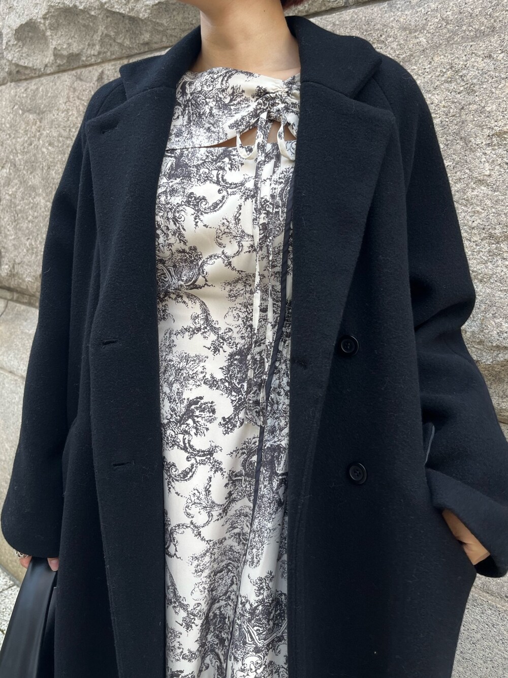 ホワイト系のワンピース、ブラック系のチェスターコート、ブラック系のハンドバッグを着用したレディースの冬コーディネートの6枚目の写真