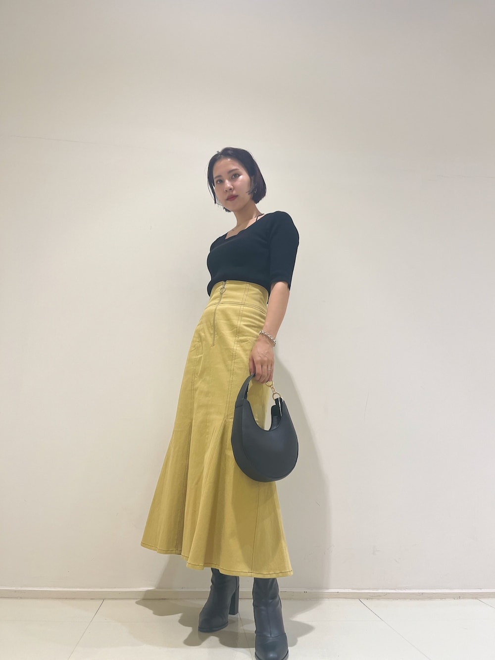 イエロー系のスカート、ブラック系のハンドバッグ、ブラック系のニット/セーターを着用したレディースの秋コーディネートの4枚目の写真
