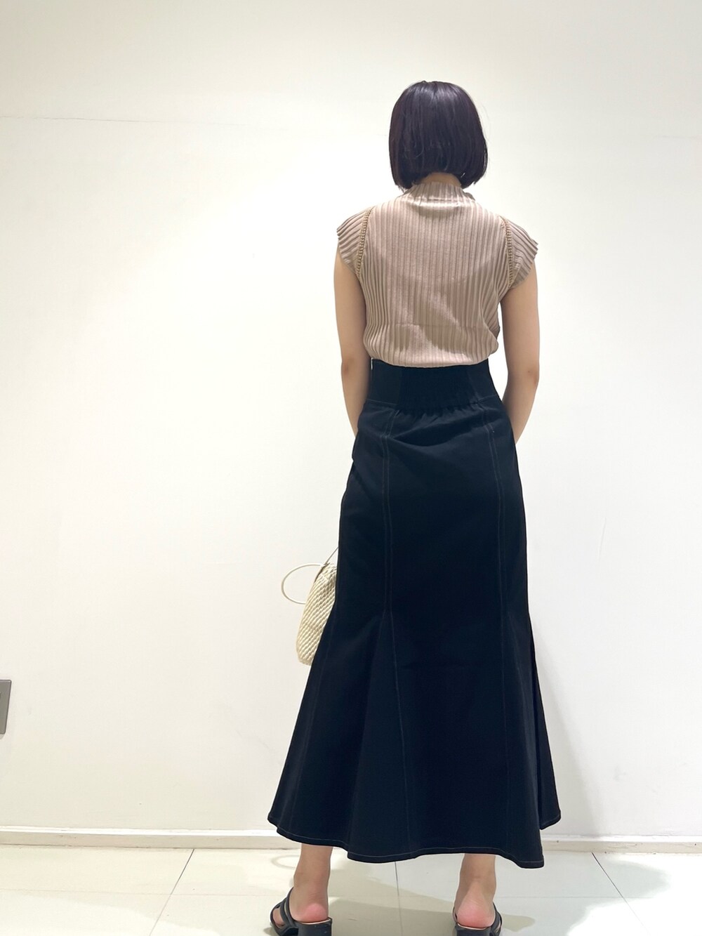 ブラック系のスカート、ベージュ系のニット/セーター、ホワイト系のハンドバッグを着用したレディースの夏コーディネートの3枚目の写真