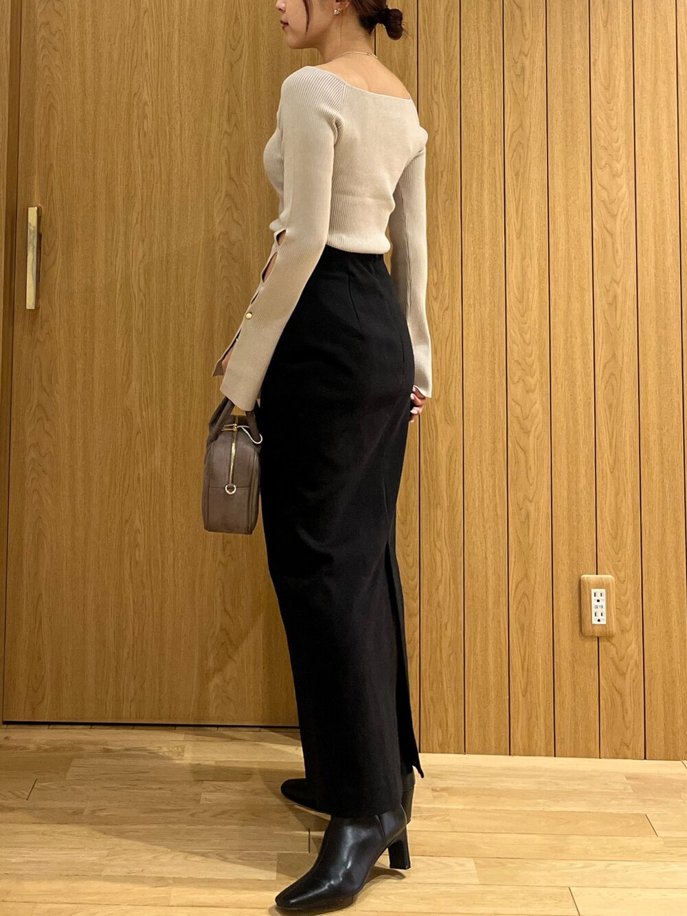 ブラック系のスカート、ベージュ系のニット/セーター、ブラウン系のハンドバッグを着用したレディースの秋コーディネートの2枚目の写真