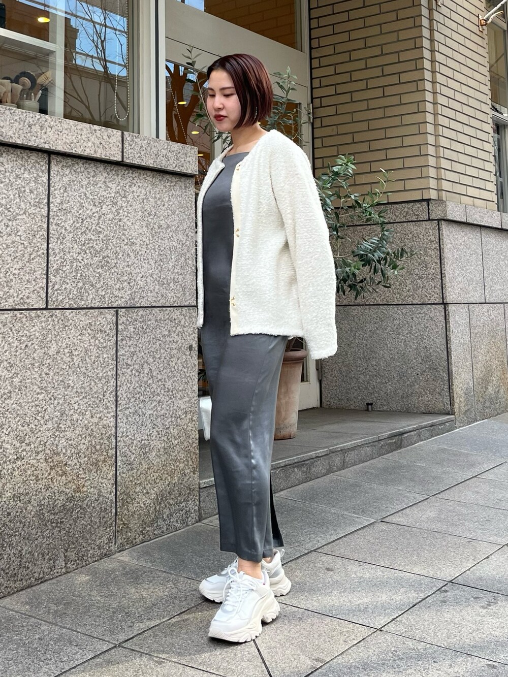 シルバー系のハンドバッグ、ホワイト系のスニーカー、グレー系のワンピースを着用したレディースの春コーディネートの2枚目の写真