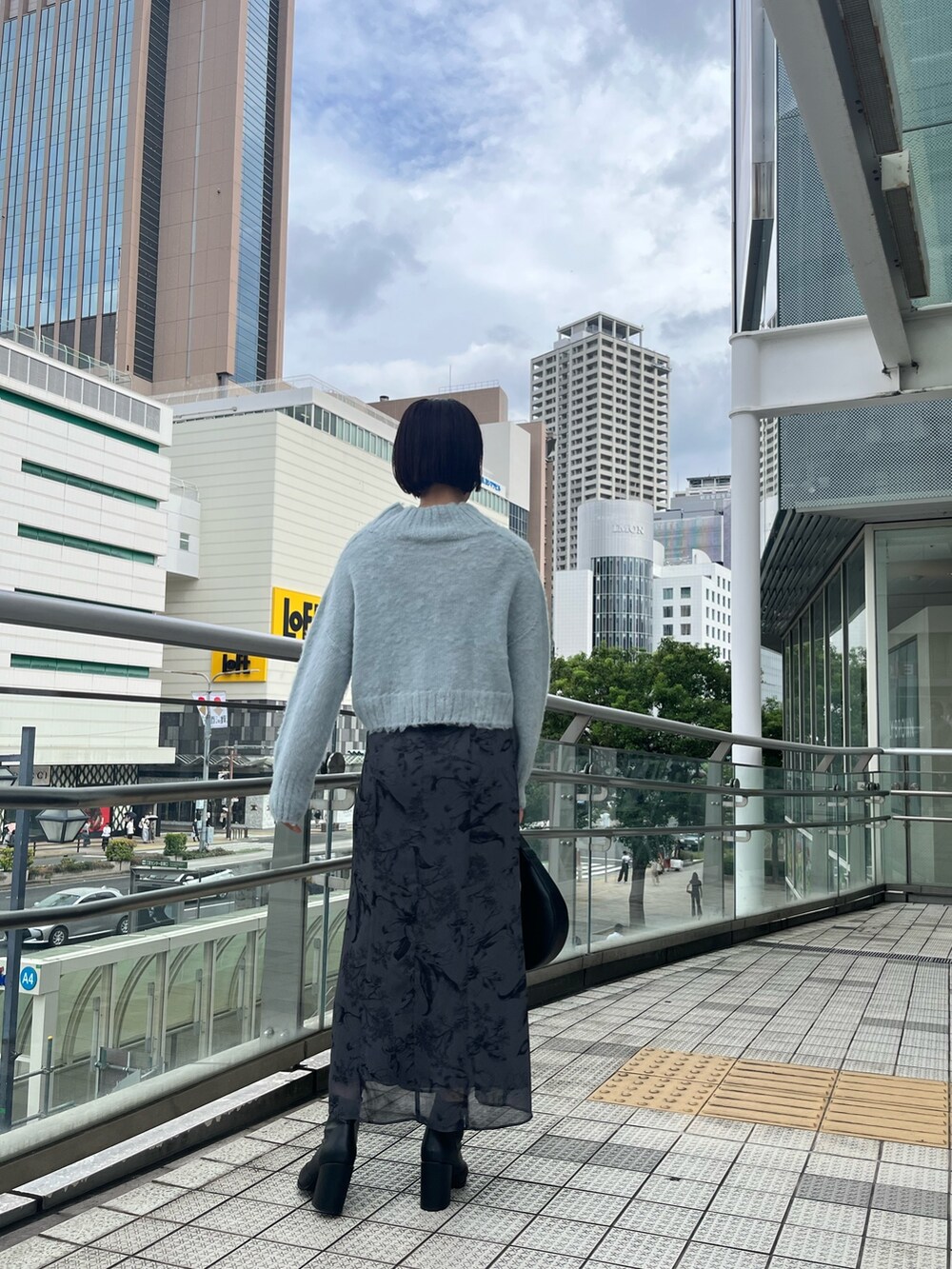 グリーン系のニット/セーター、ブラック系のハンドバッグ、グレー系のスカートを着用したレディースの秋コーディネートの2枚目の写真