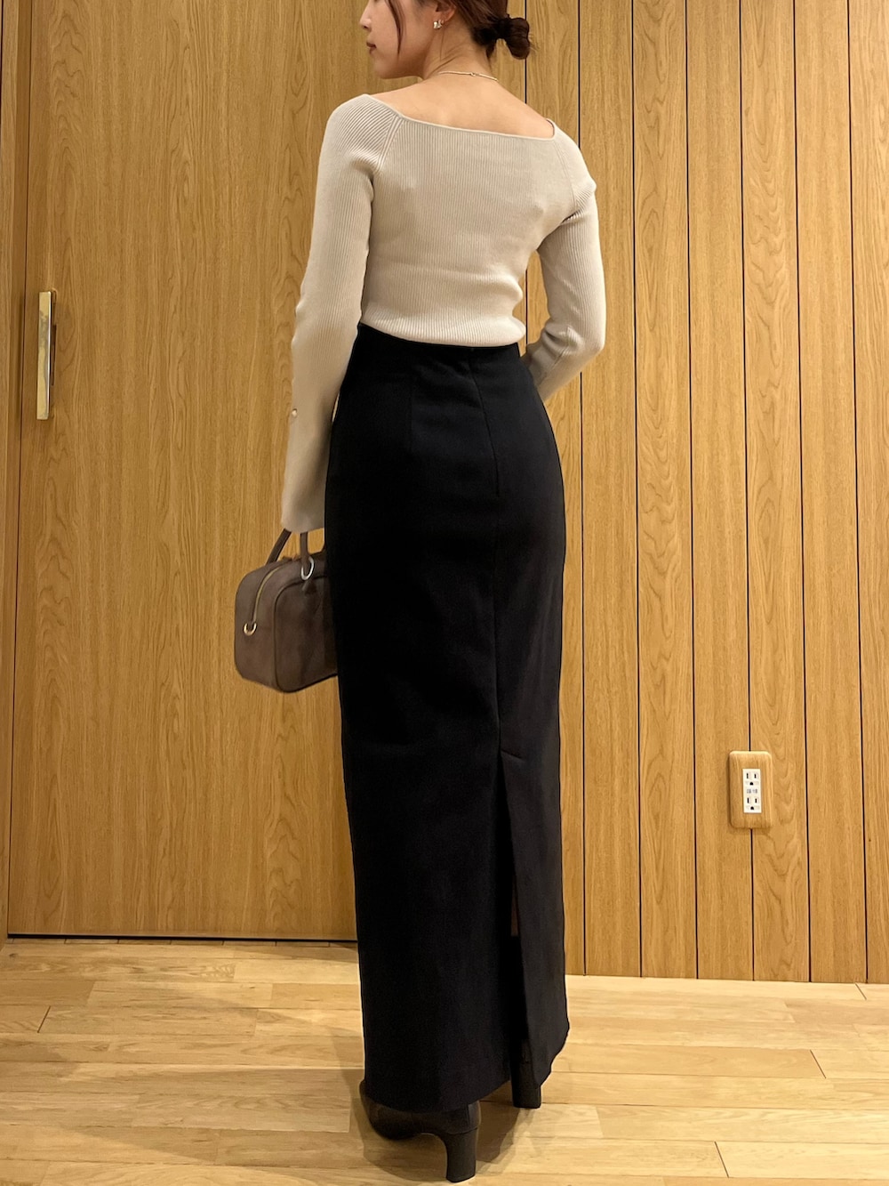 ブラック系のスカート、ベージュ系のニット/セーター、ブラウン系のハンドバッグを着用したレディースの秋コーディネートの3枚目の写真