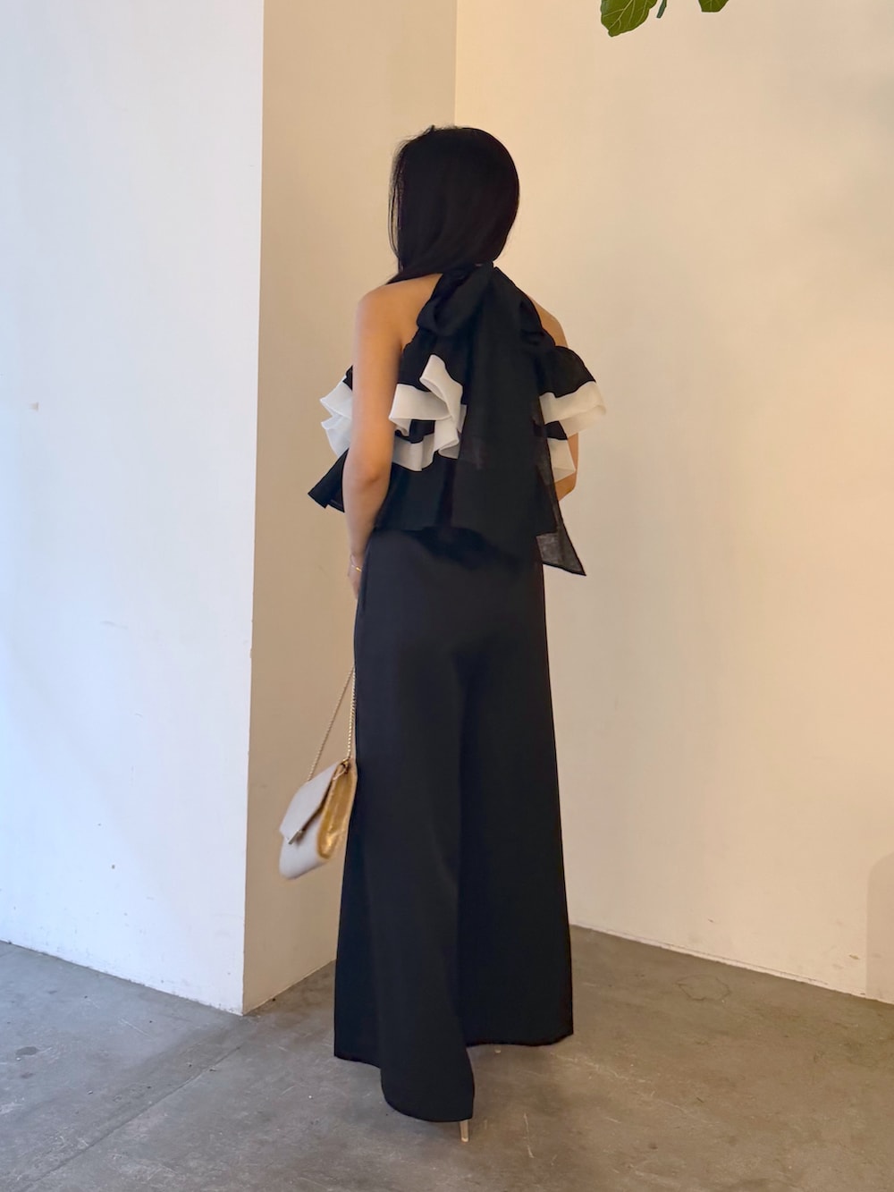 ブラック系のパンツドレス、ゴールド系のパンプス、ゴールド系のクラッチバッグを着用したレディースの夏コーディネートの3枚目の写真