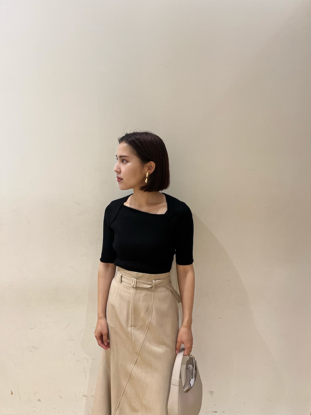 ベージュ系のスカート、ブラック系のニット/セーター、ホワイト系のハンドバッグを着用したレディースの夏コーディネートの5枚目の写真