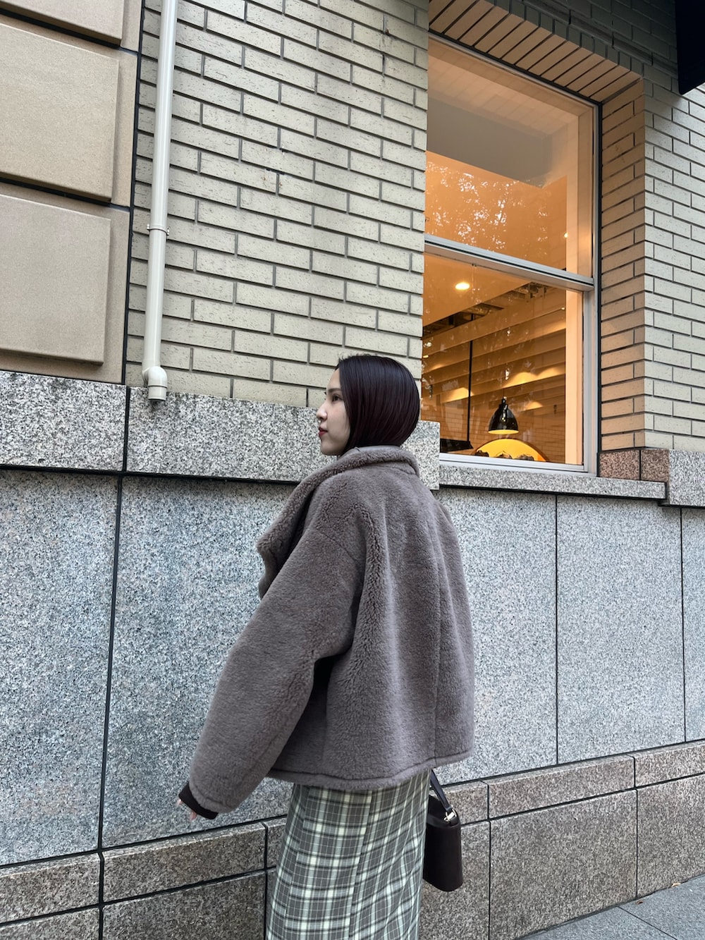 ベージュ系のムートンコート、ブラウン系のTシャツ/カットソー、ブラウン系のスカートを着用したレディースの冬コーディネートの7枚目の写真