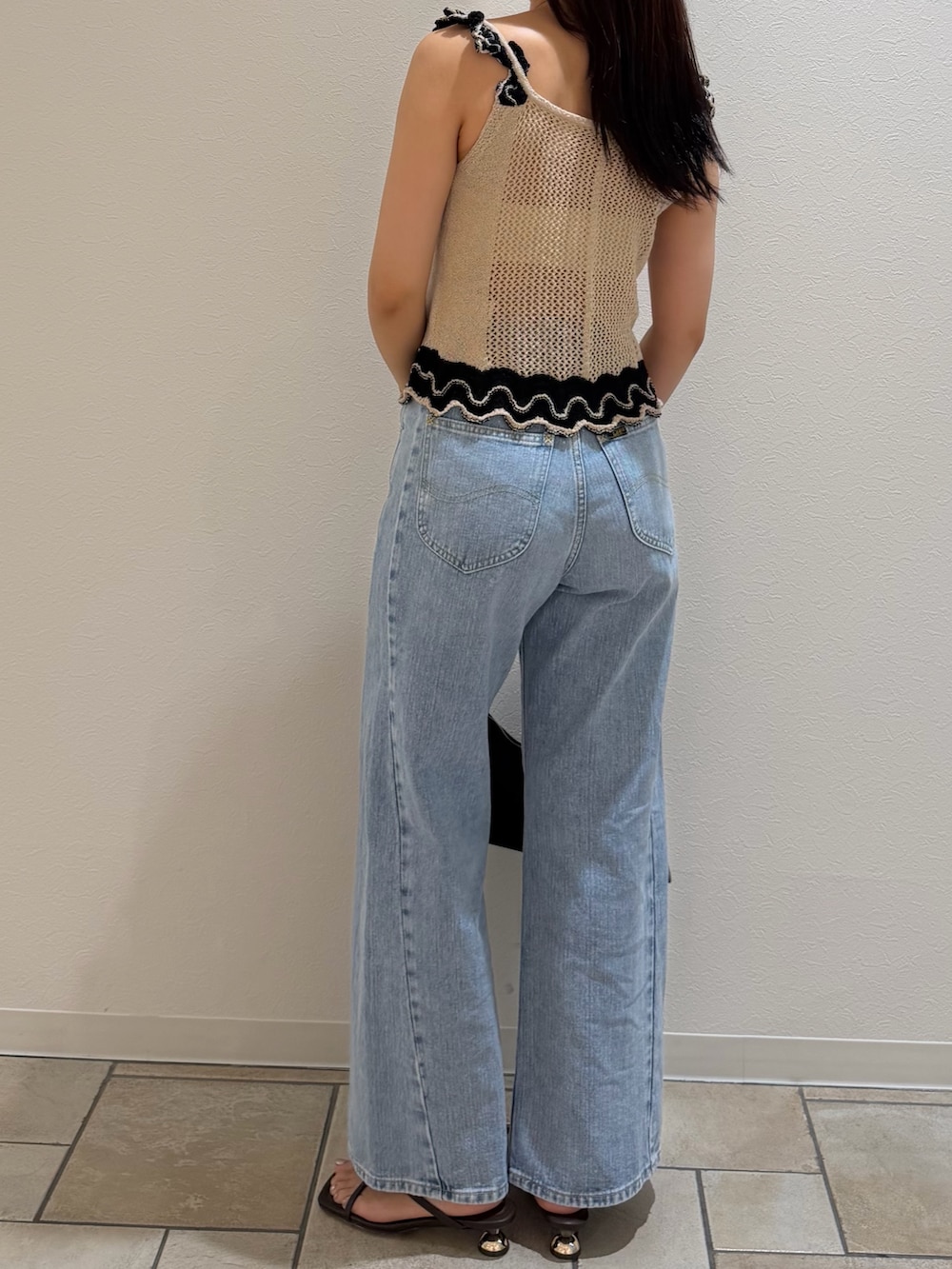 ブルー系のデニムパンツ、ベージュ系のニット/セーター、ブラック系のハンドバッグを着用したレディースの夏コーディネートの3枚目の写真