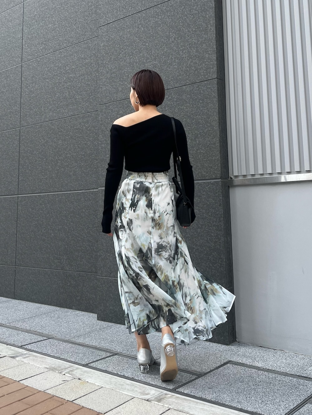 ブルー系のスカート、シルバー系のパンプス、ブラック系のハンドバッグを着用したレディースの春コーディネートの4枚目の写真