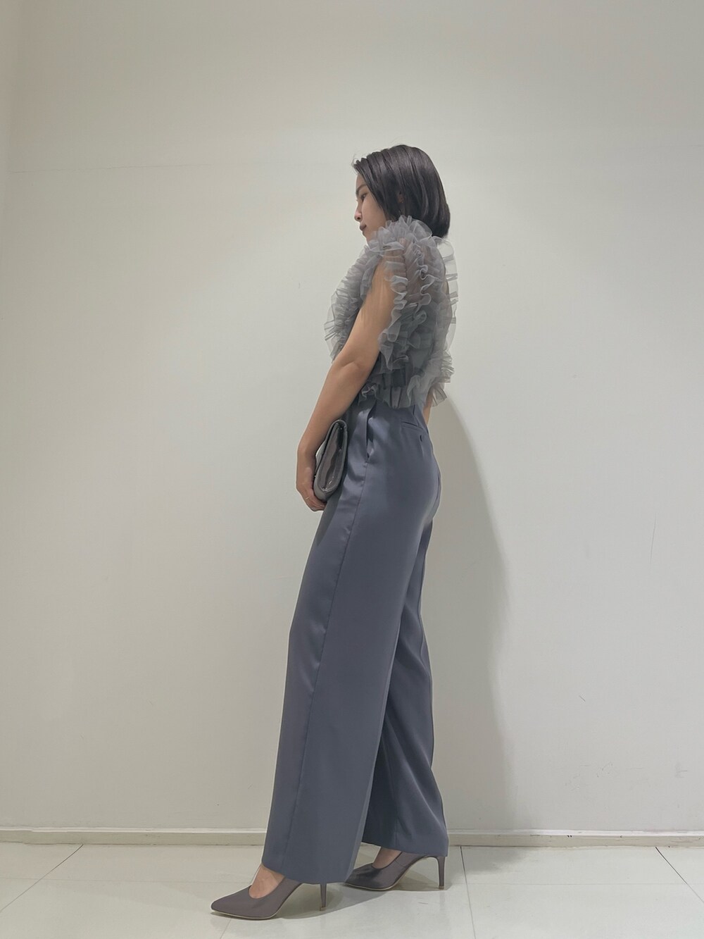 シルバー系のハンドバッグ、シルバー系のパンプス、グレー系のパンツドレスを着用したレディースの春コーディネートの3枚目の写真