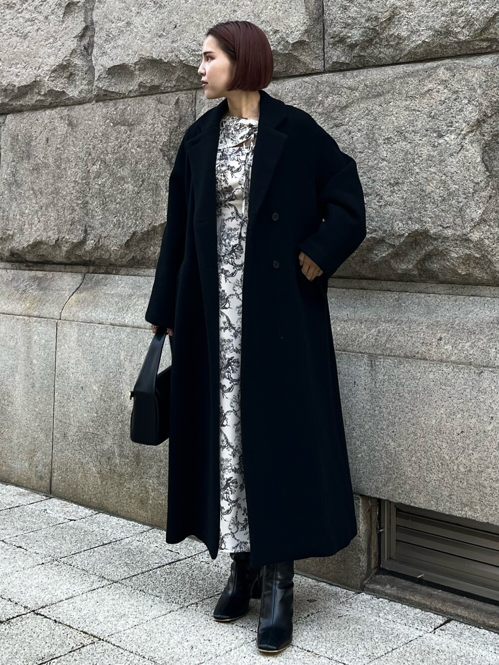 ホワイト系のワンピース、ブラック系のチェスターコート、ブラック系のハンドバッグを着用したレディースの冬コーディネートの3枚目の写真