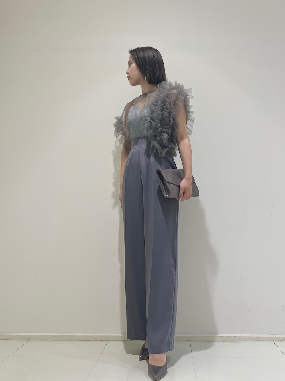 シルバー系のハンドバッグ、シルバー系のパンプス、グレー系のパンツドレスを着用したレディースの春コーディネートの2枚目の写真