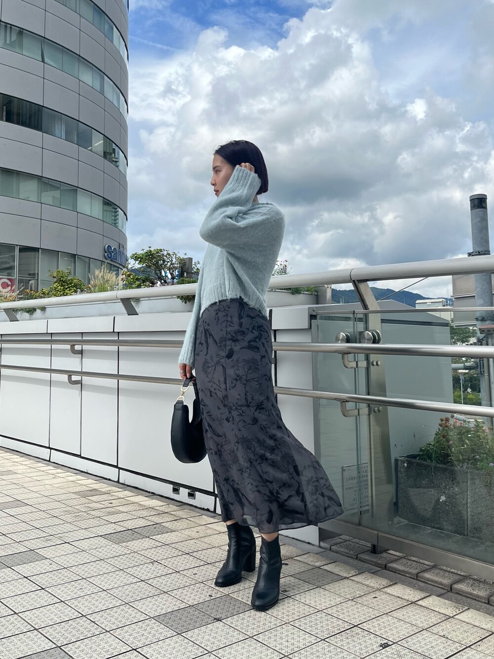 グリーン系のニット/セーター、ブラック系のハンドバッグ、グレー系のスカートを着用したレディースの秋コーディネートの3枚目の写真