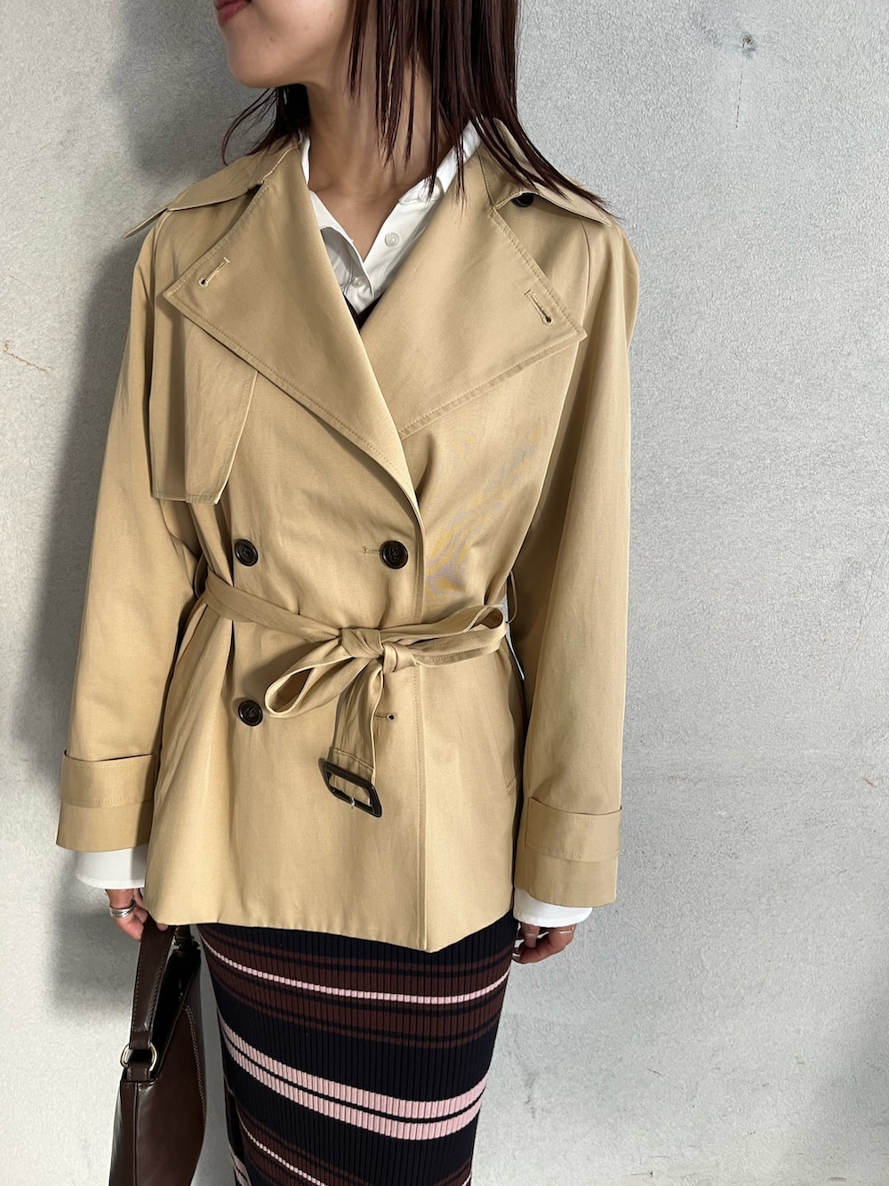 ブラウン系のハンドバッグ、ブラウン系のワンピース、ベージュ系のトレンチコートを着用したレディースの冬コーディネートの5枚目の写真