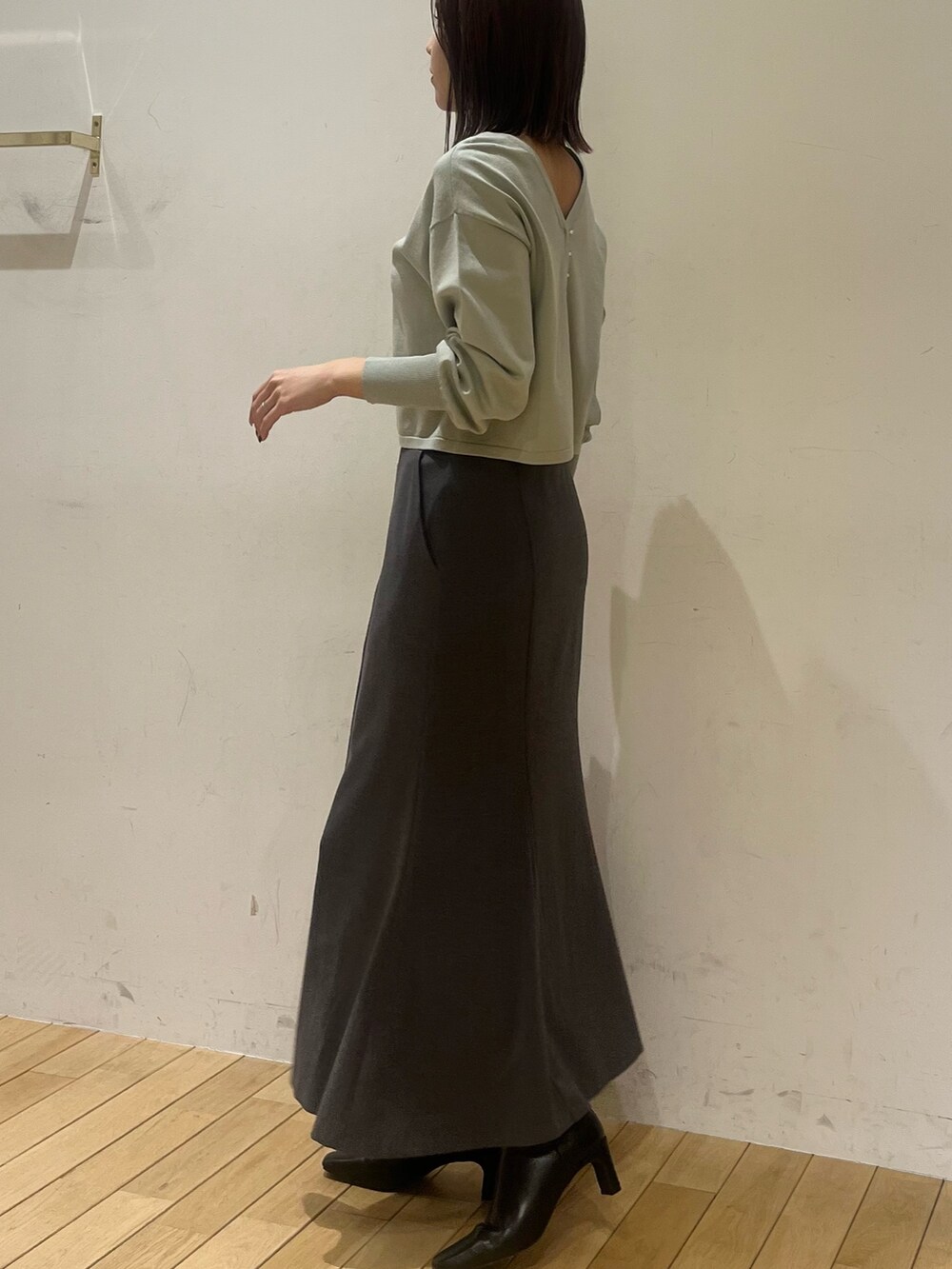 グリーン系のニット/セーター、グレー系のスカート、ブラック系のブーツを着用したレディースの冬コーディネートの2枚目の写真