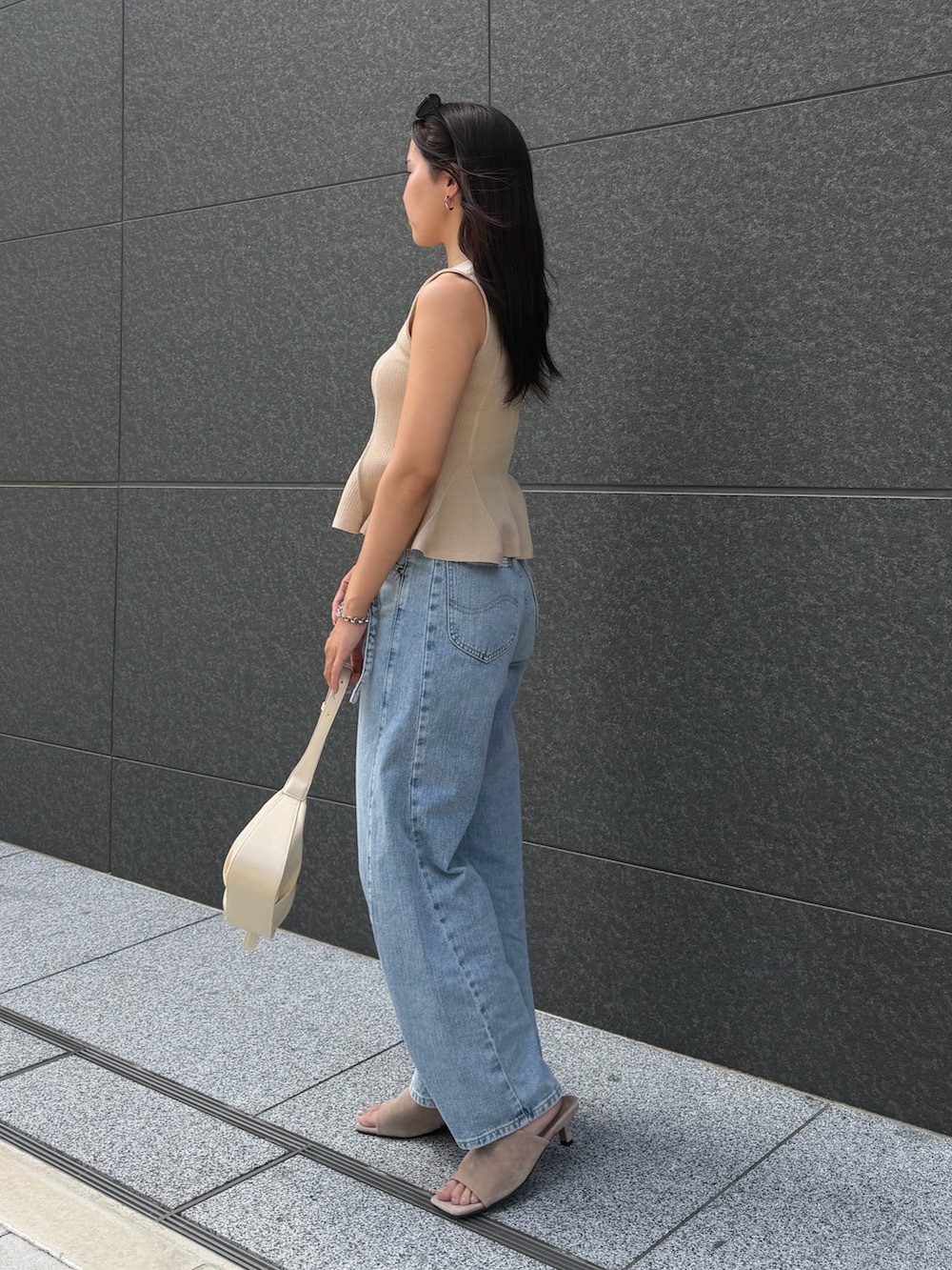 ブルー系のデニムパンツ、ベージュ系のニット/セーター、ホワイト系のハンドバッグを着用したレディースの夏コーディネートの2枚目の写真