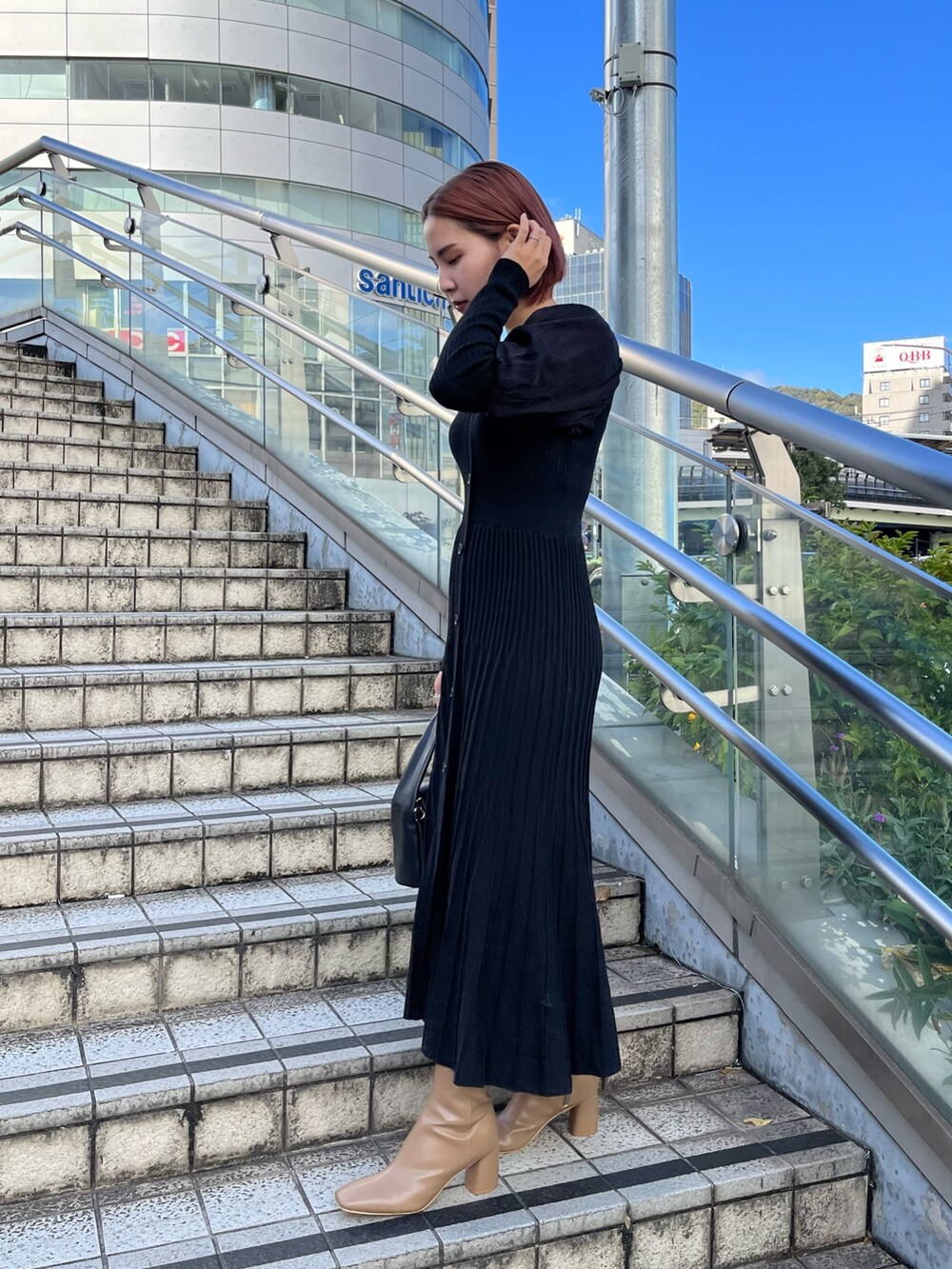 ブラック系のワンピース、ブラック系のハンドバッグ、ベージュ系のブーツを着用したレディースの秋コーディネートの2枚目の写真